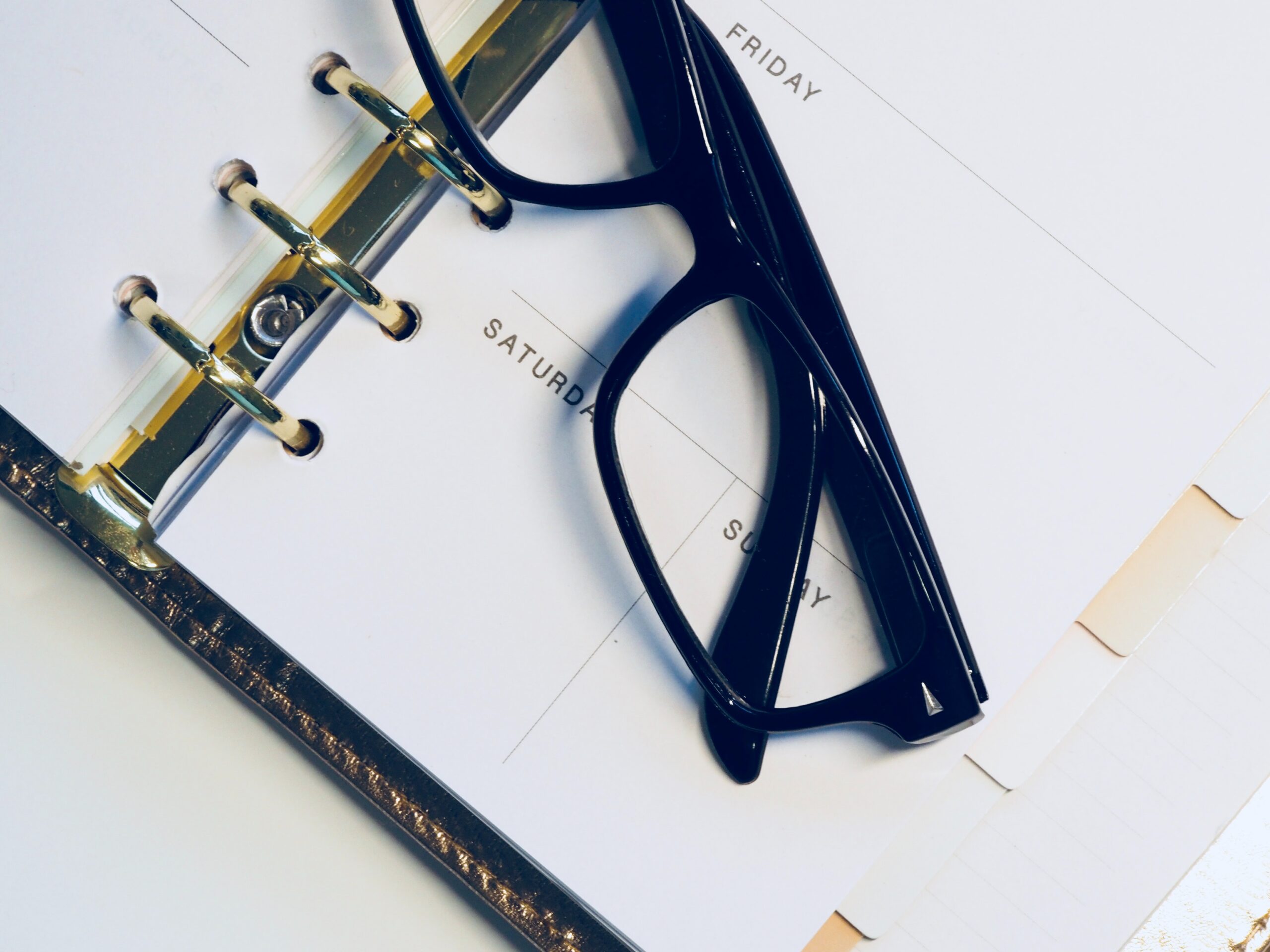 folded pair of reading glasses with thick black frames, resting across a day planner